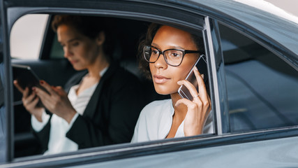 Young executive talking on a cell phone. Two businesswomen sitting on a backseat of a taxi.