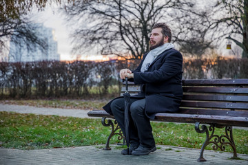 Naklejka na ściany i meble middle adult bearded man portrait sitting on wooden bench in black coat melancholy mood in autumn park outdoor space 