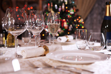 A glass of champagne, half filled, stands on a beautifully laid table.The concept of the celebration. The Christmas tree is out of focus. Flank. Copy space.