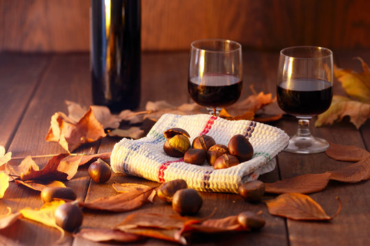 an autumn time still life with a bottle and a glass of red wine and roasted chestnuts wrapped in an old dish towel