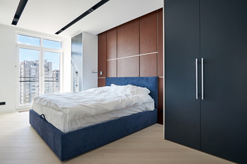Modern bedroom with fitted wardrobes, a double bed with a cushioned headboard and the wall behind him decorated with veneer walnut