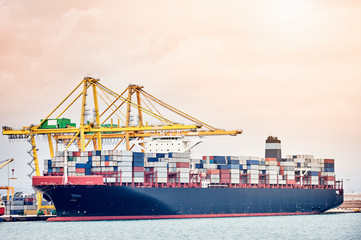 Ship-to-shore cranes loading containers on vessel in harbor enviroment. Transportation industry and shipment logistics. Export and import bussines