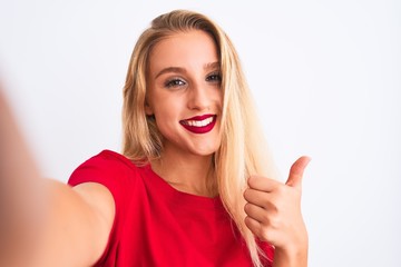 Young beautiful woman wearing t-shirt make selfie by camera over isolated white background happy with big smile doing ok sign, thumb up with fingers, excellent sign