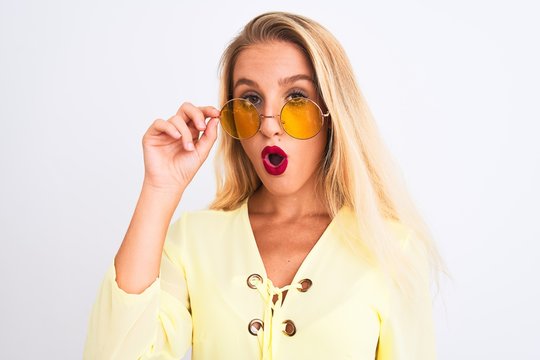 Young beautiful woman wearing yellow t-shirt and sunglasses over isolated white background scared in shock with a surprise face, afraid and excited with fear expression