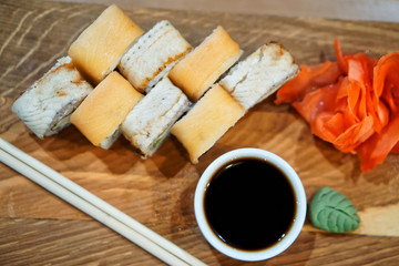 Sushi Rolls with rice, salmon, eel, wassabi, soy sauce and ginger on a wooden table, next to wooden chopsticks. Healthy food. Restaurant. Shallow depth of field.