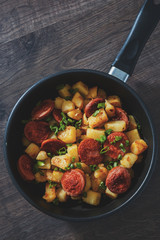 Roasted Potato and Sausage in frying pan on wooden table. Top view with copy space