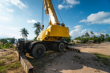 Obraz premium Yellow automobile crane with risen telescopic boom outdoors. Mobile construction crane on a constructin site. Crane machine stand by waiting for work under the construction building. Heavy industry.