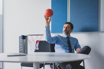 Mature businessman playing basketball in office