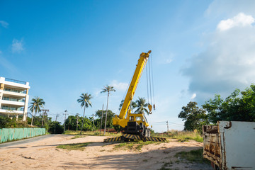 Yellow automobile crane with risen telescopic boom outdoors. Mobile construction crane on a constructin site. Crane machine stand by waiting for work under the construction building. Heavy industry.