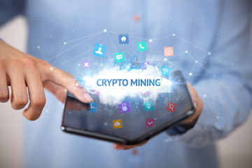 Businessman holding a foldable smartphone with CRYPTO MINING inscription, technology concept