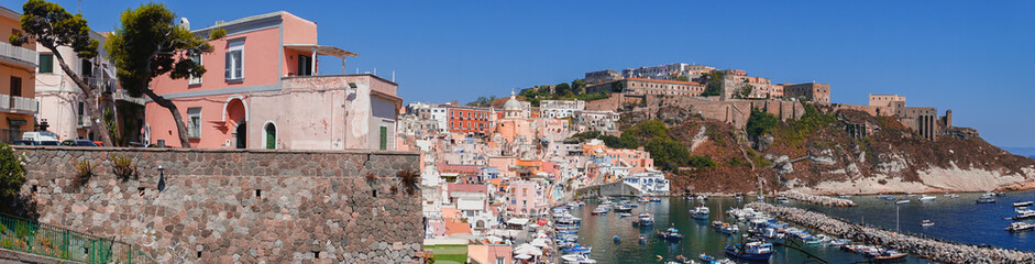 Fototapeta na wymiar Panoramic view of beautiful Procida on a sunny summer day. Colorful cafes, houses and restaurants, fishing boats and yachts, clear blue sky and the azure sea on the island of Procida, Italy. Napoli