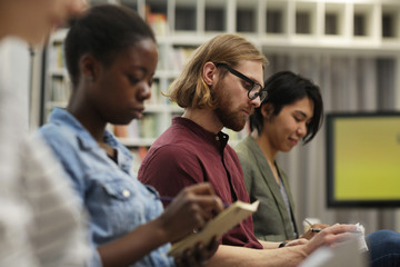 Multiethnic group of serious students concentrating on their writing while they sitting at lecture