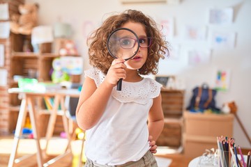Beautiful toddler standing  wearing glasses using loupe at kindergarten