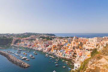 Naklejka na ściany i meble Panoramic view of beautiful Procida on a sunny summer day. Colorful cafes, houses and restaurants, fishing boats and yachts, clear blue sky and the azure sea on the island of Procida, Italy. Napoli
