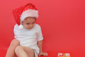 Portrait of child boy in Santa red hat looking Christmas gift the red background