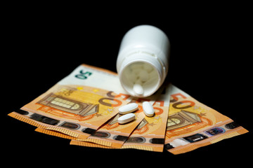 Pills pour out of a pill bottle on the euro banknotes, representing the high cost of health care and medication concepts.  Isolated on black.