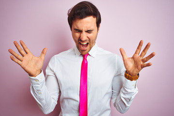 Young handsome businessman wearing shirt and tie standing over isolated pink background celebrating mad and crazy for success with arms raised and closed eyes screaming excited. Winner concept
