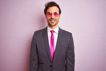 Young handsome businessman wearing suit and sunglasses over isolated pink background with a happy and cool smile on face. Lucky person.