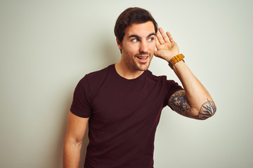 Young handsome man with tattoo wearing purple casual t-shirt over isolated white background smiling...