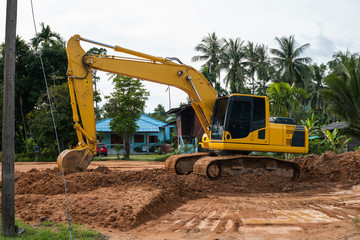 Yellow excavator on a construction site against blue sky. Heavy industry. Close up details of industrial excavator. Large tracked excavator standing on a orange ground with a palms on background.