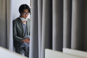 Asian young man in eyeglasses and with headphones busy reading a book