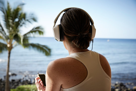 USA, Hawaii, Woman With Headphones And Smartphone In Front Of The Sea, Back View