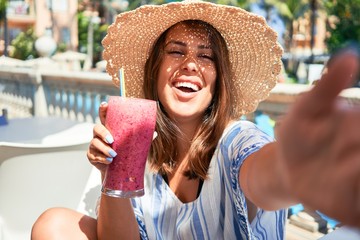 Beutiful woman sitting at pool bar on hotel resort drinking healthy smoothie and taking selfie using smartphone