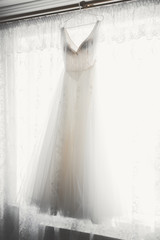The perfect wedding dress with a full skirt on a hanger in the room of the bride
