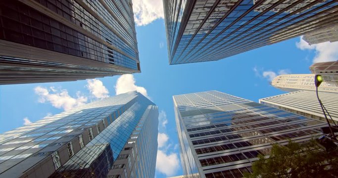 Corporate buildings, low angle panning view on NYC skyscrapers, blue sky and glass mirrored facades