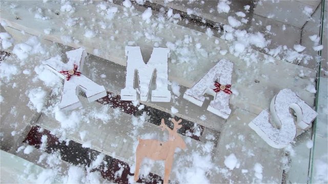 word "Xmas" and deer on glass table with snow