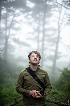 Portrait of photographer looking up into trees holding camera