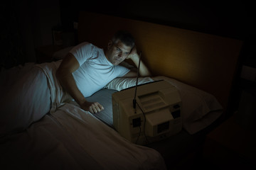 A man watches an old television on the bed at night in the dark.