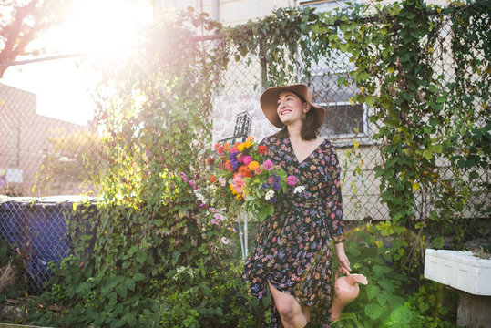 Happy Woman Holding Flowers In Urban Garden
