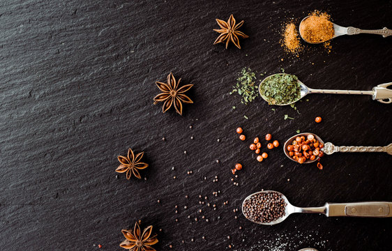 A selection of spices on vintage spoons on a slate chopping board