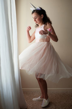 Girl 10-12 years old twirling by window dressed in fancy pink dress