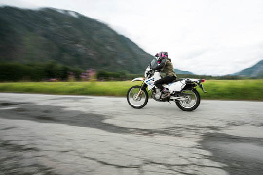 A woman rides her motorcycle on a cloudy summer day.