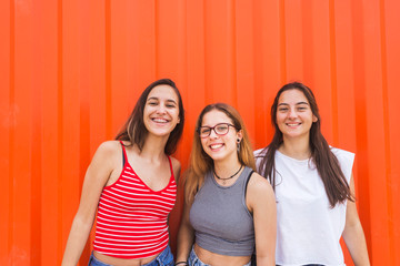 Three young happy teenage girls have fun against orange wall