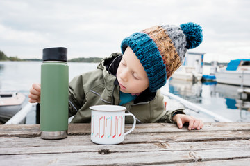 young boy sat by the beach drinking hot chocolate on a picnic bench