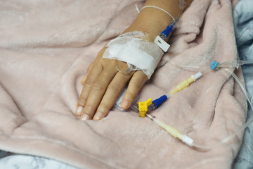 Blurry of Saline intravenous drip on hand on bed in hospital background