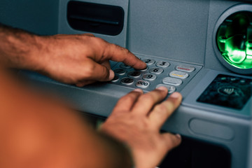 Unrecognizable close up man hands type secret pin code  in a atm bank to withdraw money - information security private concept