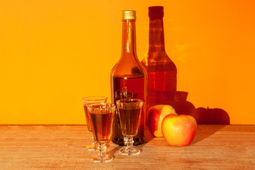 A bottle of French Calvados filled with wineglasses and apples stand on a table