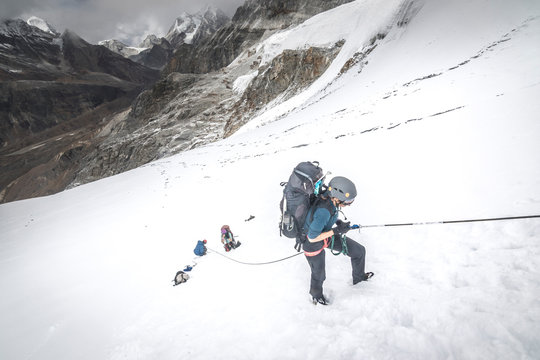 A woman climber ascends a fixed line on a steep snow slope