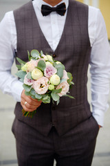 Close up of beautiful bridal bouquet of purple, pink and cream flowers and greenery in groom's hand outdoors, copy space. Wedding concept