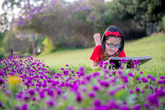The girls wear cute glasses while reading books at the park in the evening with the sunset light.