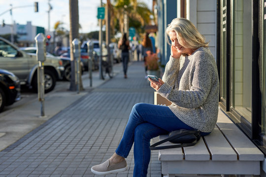 Side view of senior woman using smart phone while sitting on bench in city