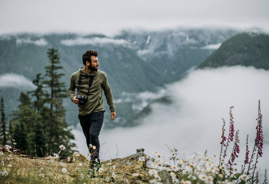 A male hiker with camera walks along a misty trail in the cascades