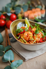 Bowl of stir fried udon noodles garnished with black sesame seeds and fresh mint with green chopsticks
