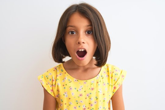 Young beautiful child girl wearing yellow floral dress standing over isolated white background scared in shock with a surprise face, afraid and excited with fear expression