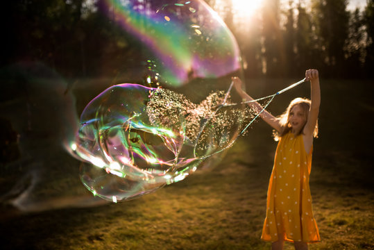 9 year old girl making giant bubble in summer light