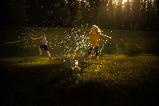 Siblings running through bubbles in golden light